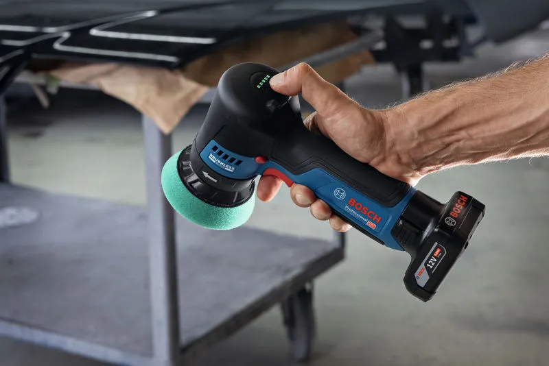 A person uses a cordless polisher with a green foam pad near a workbench.