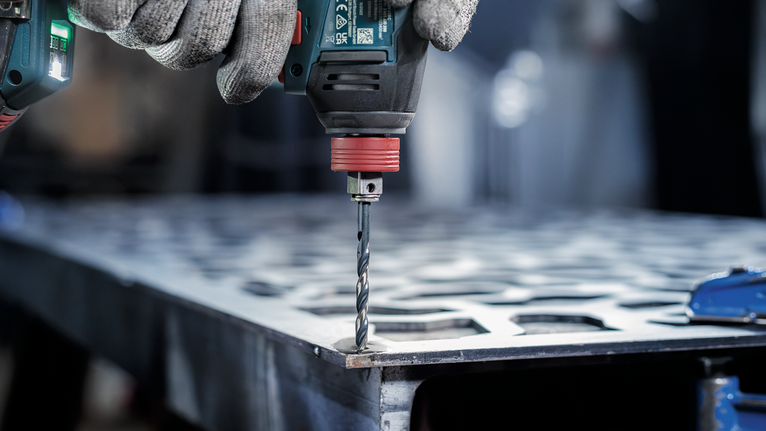 Person wearing safety equipment drills holes in a metal sheet.