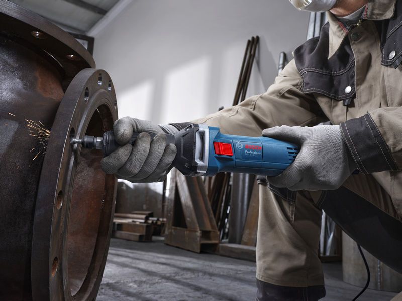 A person wearing safety equipment uses a straight grinder to grind the inside of a large metal pipe.