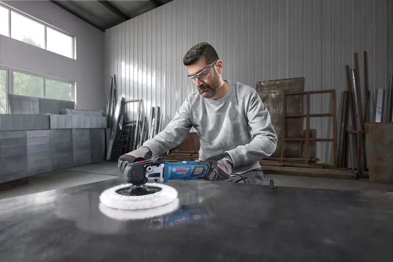 A person wearing safety equipment uses a polisher on a large metal surface.