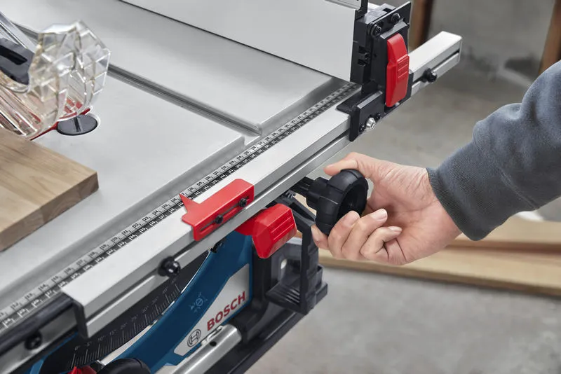 Person adjusts table saw fence using a black knob in a workshop.