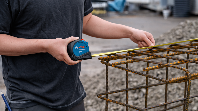 Person measuring a metal rebar frame at a construction site.