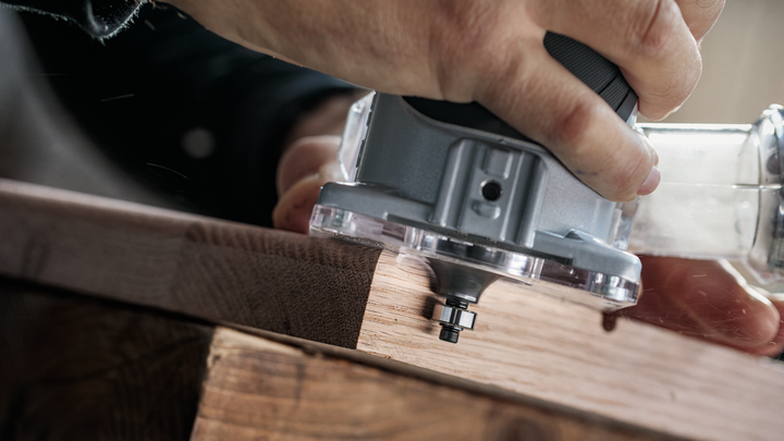 Person guiding a power trimmer along the edge of a wooden board.