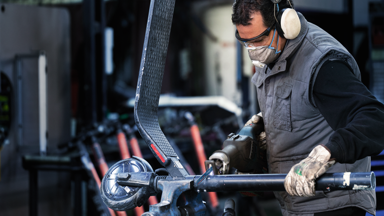 A person wearing safety equipment uses a power tool to cut metal tubing.
