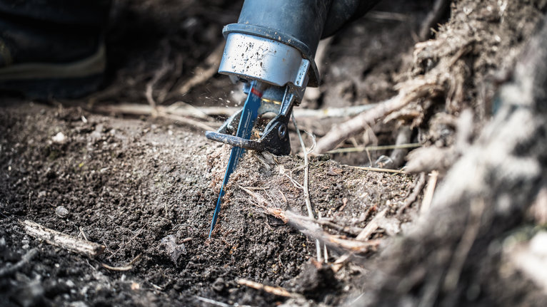 Reciprocating saw blade cutting through soil and tree roots.