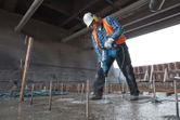 A person wearing safety equipment drills into concrete with a rotary hammer.