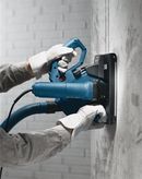 Person wearing safety equipment operates a wall chaser to cut a groove in concrete.