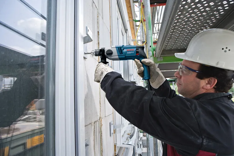 A person wearing safety equipment drills into a concrete wall on a construction site.