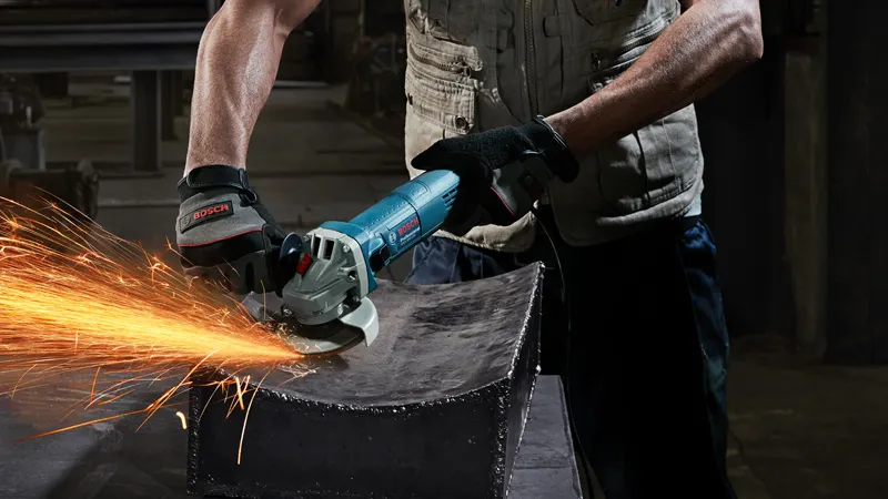 A person wearing safety equipment grinds metal, producing bright sparks.