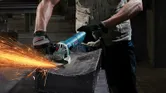 A person wearing safety equipment grinds metal, producing bright sparks.