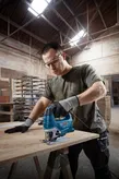 Person wearing safety equipment uses a jigsaw to cut wood in a workshop.