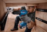 A person wearing safety equipment installs a drawer slide using a cordless drill.
