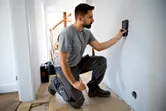A person scans a wall with a detector device in a home interior.