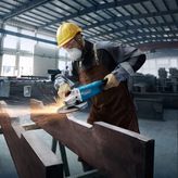 A person wearing safety equipment grinds metal with a power tool, sparks flying.
