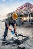 A person wearing safety equipment cuts paving blocks with a power cutter at a construction site.