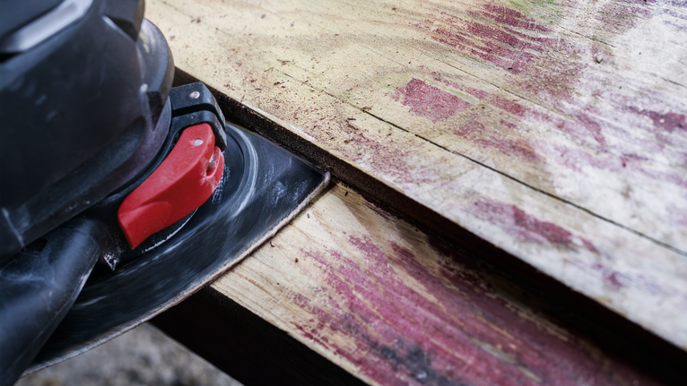 Electric sander smoothing a weathered wooden plank.