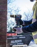 A person wearing safety equipment drills into a brick wall with a cordless power drill.