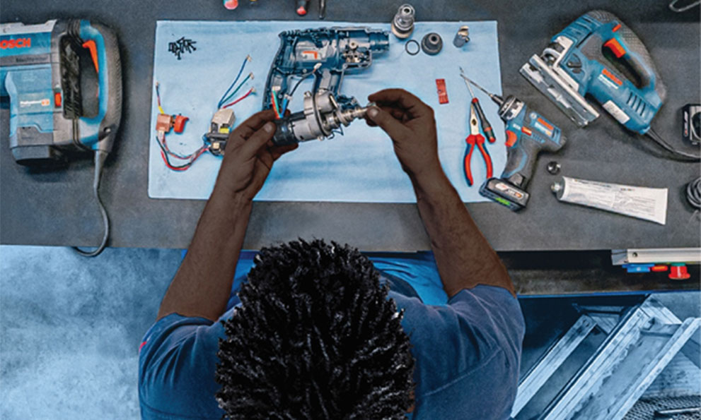 A person repairs Bosch tools on a workbench, surrounded by various parts and tools.