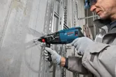 شخص يرتدي معدات السلامة يقوم بالحفر في جدار خرساني على طول الخطوط الإرشادية الزرقاء.