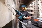 A person wearing safety equipment drills into a concrete wall at a construction site.