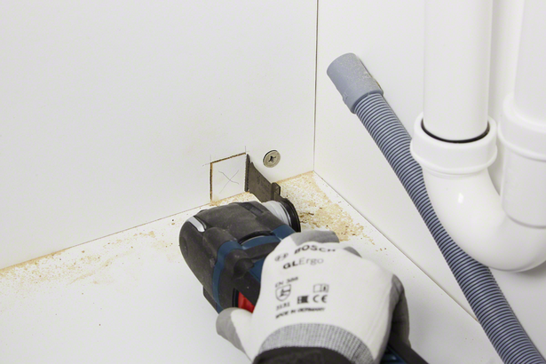 Worker wearing safety equipment cuts a square opening in a cabinet with a power tool.
