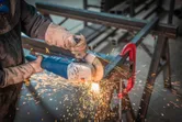 A person wearing safety equipment grinds metal with an angle grinder, producing sparks.