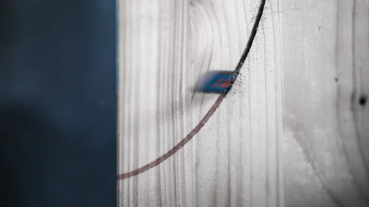 A jigsaw blade cutting a curved line through a wooden board.