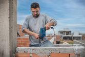 A person wearing safety equipment drills into a concrete wall at a construction site.