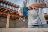 A person drills into wood with an impact drill in a construction setting.