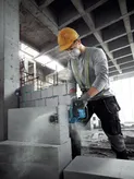 A person wearing safety equipment cuts an AAC block with a power cutter in a construction site.