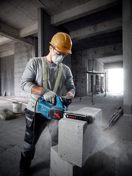 A person wearing safety equipment uses an AAC block cutter on a concrete block.