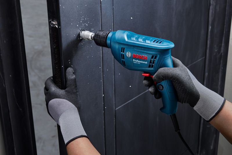 A person wearing safety equipment drills a hole into a metal wall with a power tool.