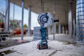 Cordless angle grinder standing upright on a concrete surface at a construction site.