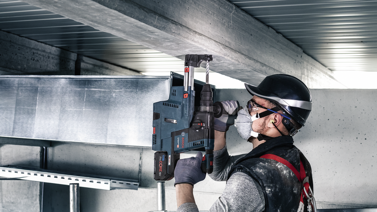 A person wearing safety equipment drills into a steel beam with a power tool.