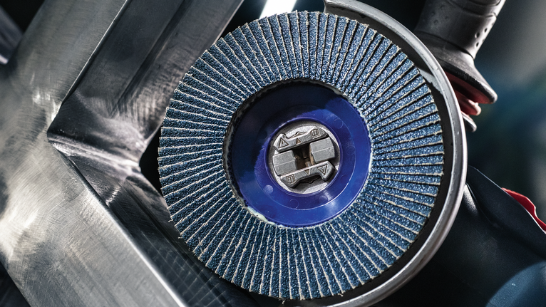 A blue flap disc grinds metal, with tool held near a steel surface.