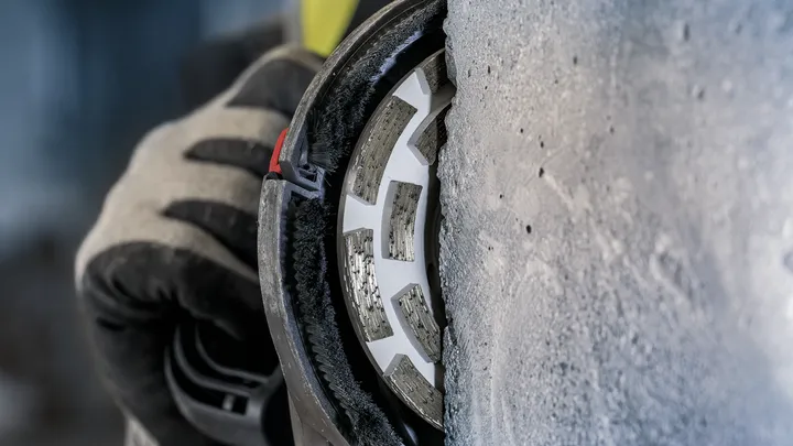 A person wearing safety equipment grinds concrete with a diamond wheel.