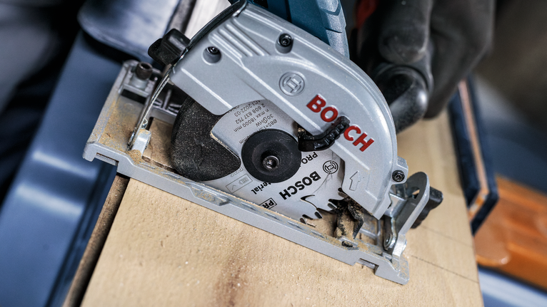 Person wearing safety equipment cuts wood using a circular saw.