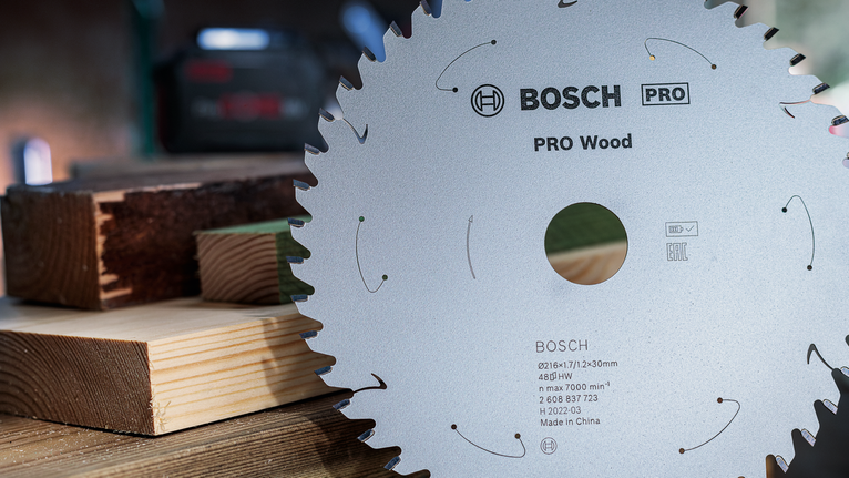 Circular saw blade with sharp teeth lies next to stacked wooden beams.