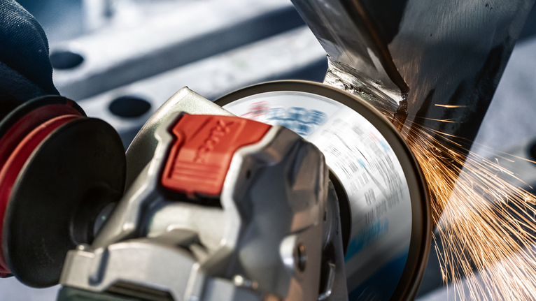 A person wearing safety equipment grinds metal, producing sparks with an angle grinder.