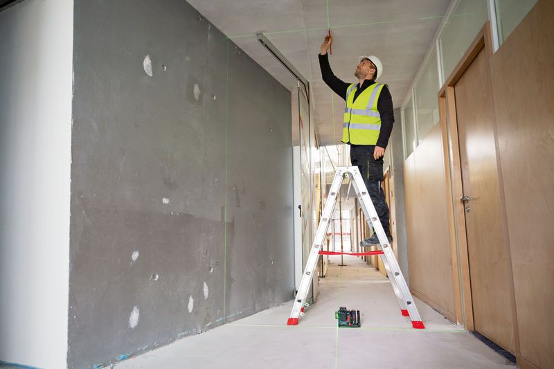 A person wearing safety equipment marks a ceiling using a laser leveling tool.