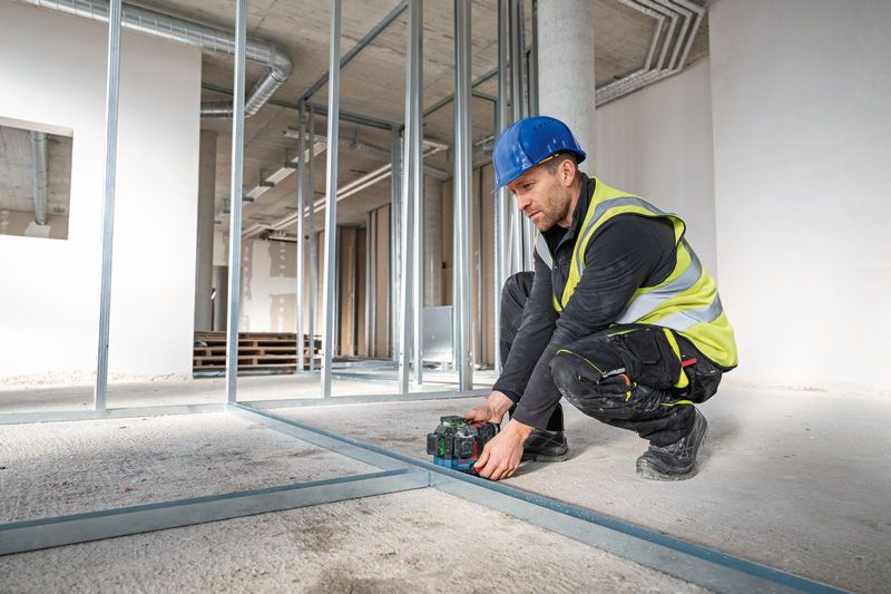 Person wearing safety equipment aligns floor track with a laser leveling tool.