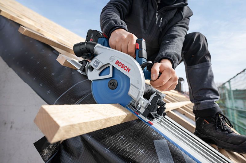 A person wearing safety equipment cuts roof timber with a cordless circular saw.