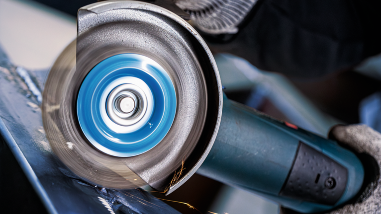 Person wearing safety equipment uses an angle grinder to cut metal.