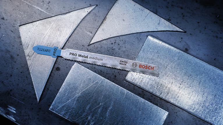 Jigsaw blade placed on a metal sheet with several cut metal pieces.
