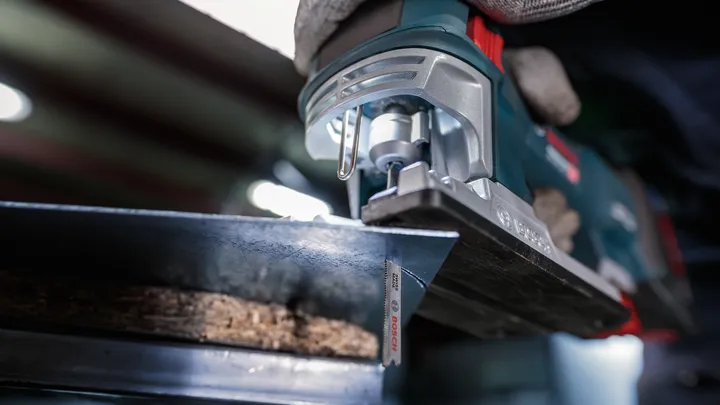 Person wearing safety equipment cuts wood with a jigsaw.