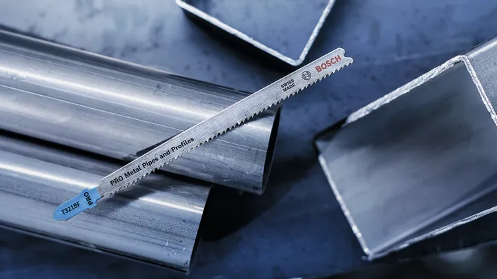 Metal saw blade resting on shiny metal pipes and square tubes.