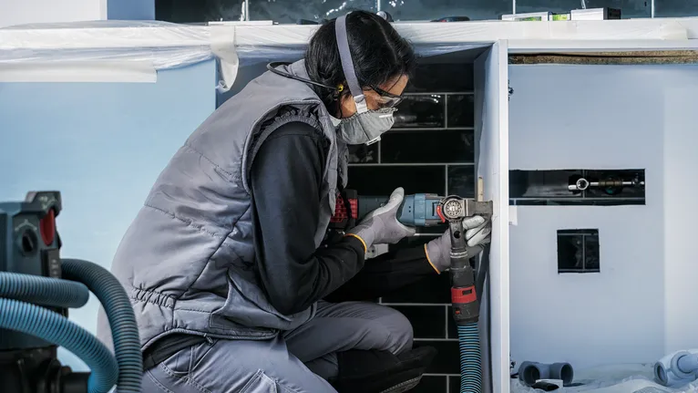 A person wearing safety equipment drills into a cabinet in a kitchen installation.