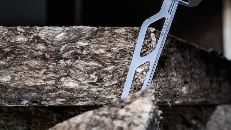 A power tool blade cutting through a thick insulation panel.