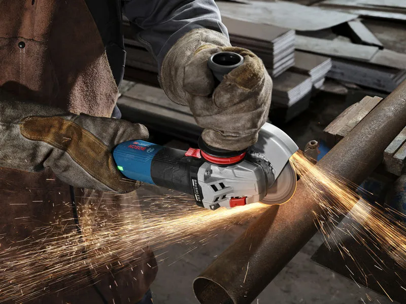 A person wearing safety equipment grinds a metal pipe with an angle grinder.