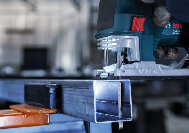 Person wearing safety equipment guides a jigsaw to cut through a metal beam.